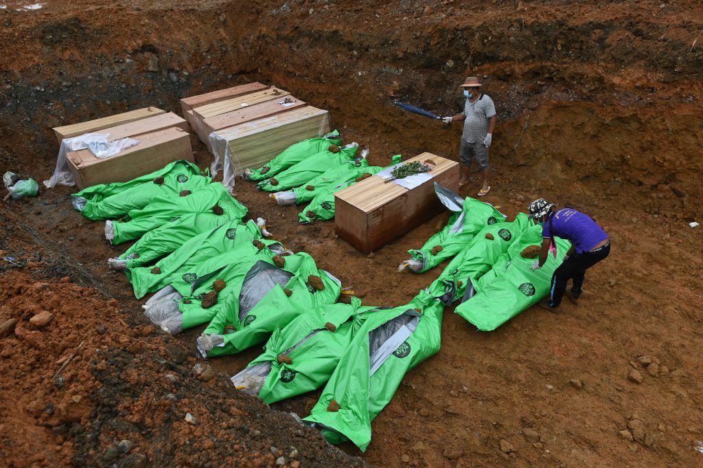 The bodies of miners in wooden coffins and wrapped up in bags are placed in a mass grave before being buried, on July 4. (AFP)