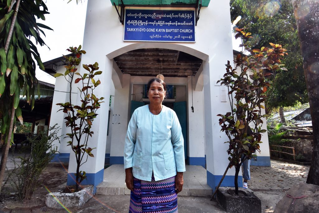 Local pastor Naw Kamu stands before Kyoe Kone's Baptist church, where the victims of the 1949 massacres are commemorated in a service each November. (Frontier)