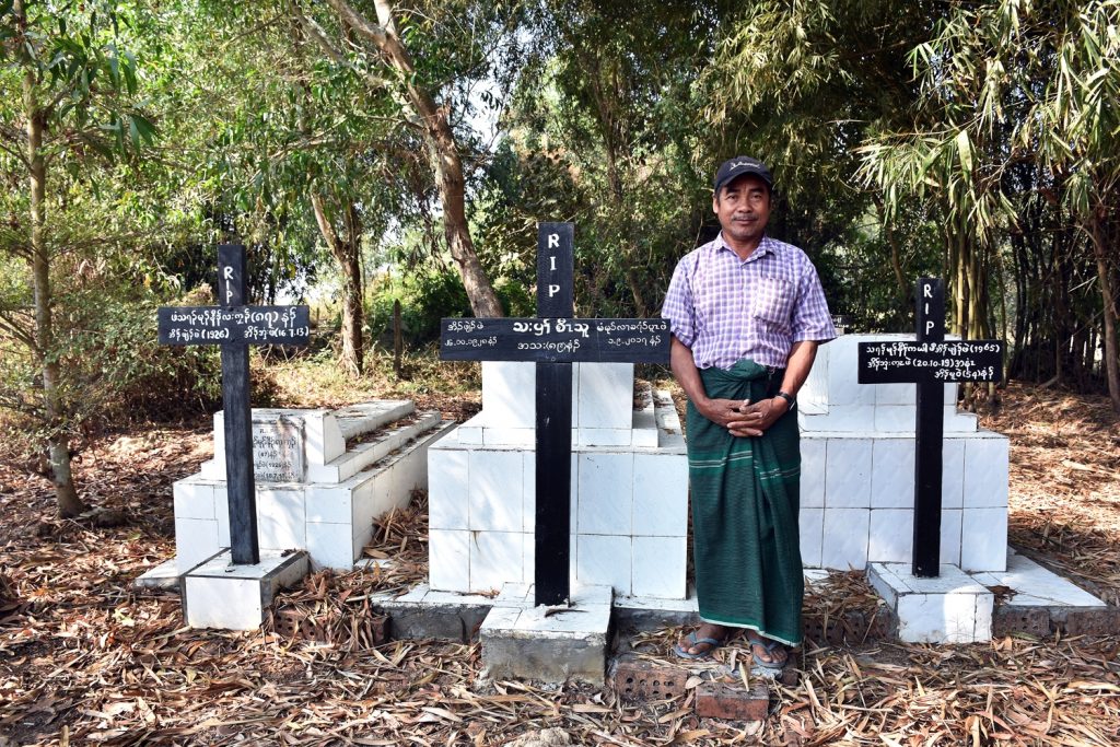 Saw Kanarni stands by the graves of his elder sister, mother and father in the Taikkyi Township village of Kyoe Kone. Kanarni’s great uncle was killed in the 1949 massacre but his body and those of others in the village were burnt by the Burmese irregular troops, and the family was unable to bury him. (Frontier)